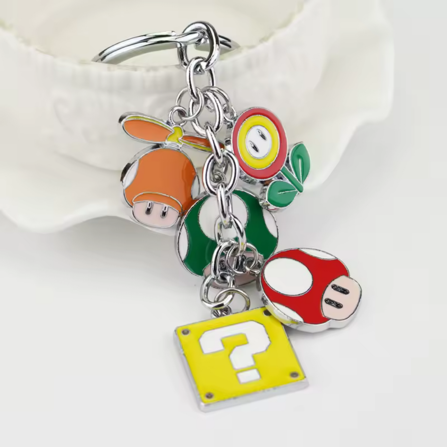 Embarque un morceau du Royaume Champignon avec ce porte-clé en chaîne ultra complet ! Il rassemble 5 icônes légendaires de l’univers Mario : le champignon vert 1-Up, le champignon rouge, la fleur de feu, le casque orange à hélice et bien sûr le mythique bloc “?”. Chaque élément est suspendu à une chaîne pour un rendu dynamique et plein de charme. Idéal pour les vrais fans et les nostalgiques du monde pixelisé de Nintendo !